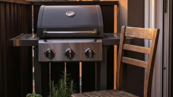 Liten kompakt gassgrill på en skandinavisk leilighetsbalkong med urtepotter og varm kveldssol